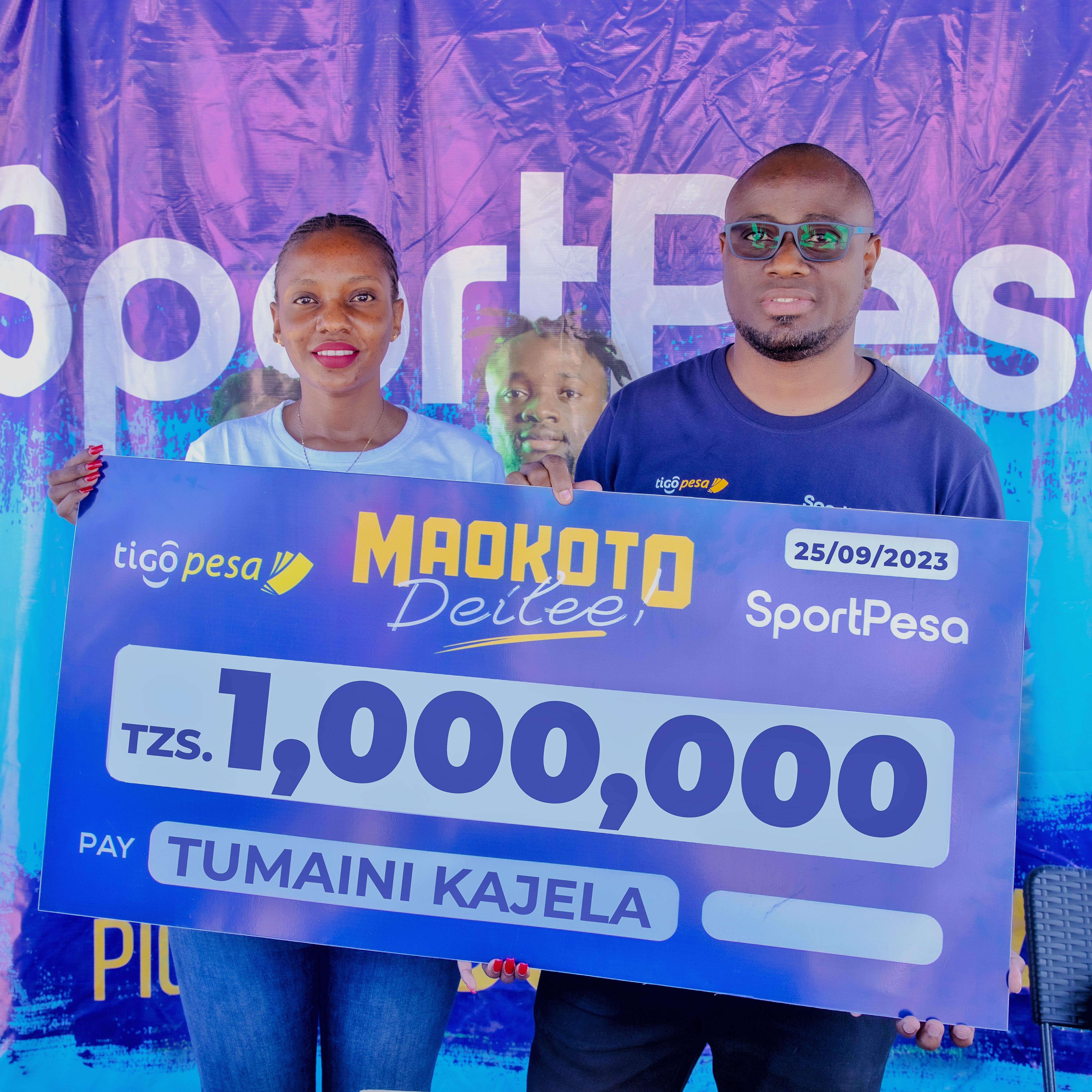 Afisa wa Mawasiliano na uhusiano kutoka sportpesa Lydia Solomon, akiwa na Meneja Biashara kutoka tigo pesa Kenneth Ndulute wakikabidhi mfano wa hundi kwa mshindi wa droo ya wiki ya Maokoto Deilee