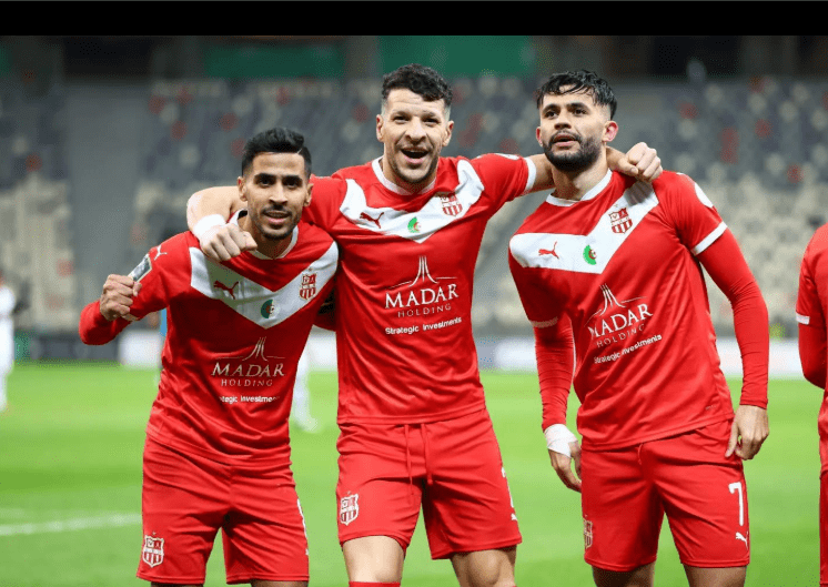 Three CR Belouizdad players in their red home kits celebrating happily on the pitch after a match.